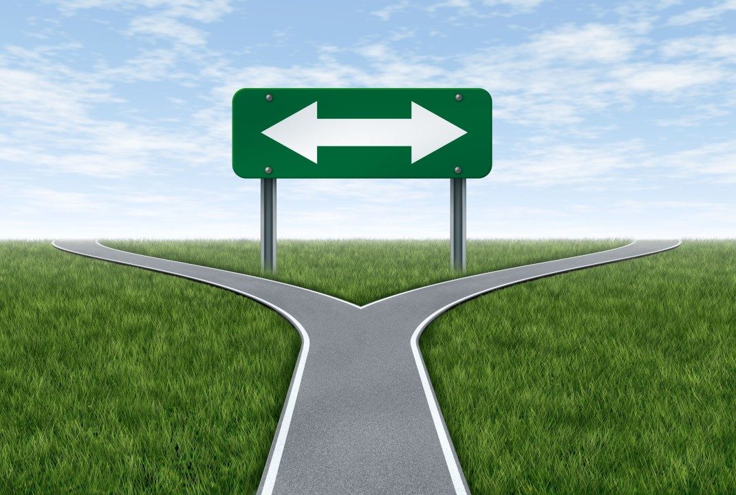 A road splitting in two beneath a double-headed arrow sign